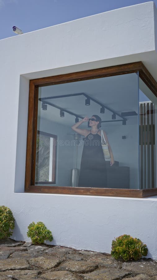 Kvinnor i svart klänning som står i ett modernt hus med stora fönster som ser ut utanför och visar samtida inredning royaltyfria bilder