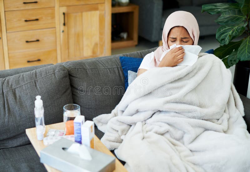 Woman, muslim and blow nose or sick in home, cold and medicine for illness and treatment for health. Female person, hijab and blanket on couch for sinus, pills and virus or hayfever and recovery. Woman, muslim and blow nose or sick in home, cold and medicine for illness and treatment for health. Female person, hijab and blanket on couch for sinus, pills and virus or hayfever and recovery.