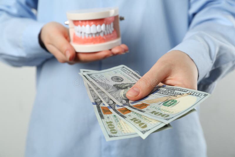 Kvinnor som innehar tandläkartypodontmodell för utbildning och dollarsedlar på ljusbakgrundsstängning. kostsam behandling fotografering för bildbyråer