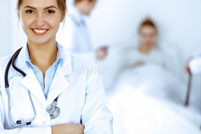 Kvinnor som leker i bakgrunden med patienten i sängen och två läkare royaltyfri fotografi