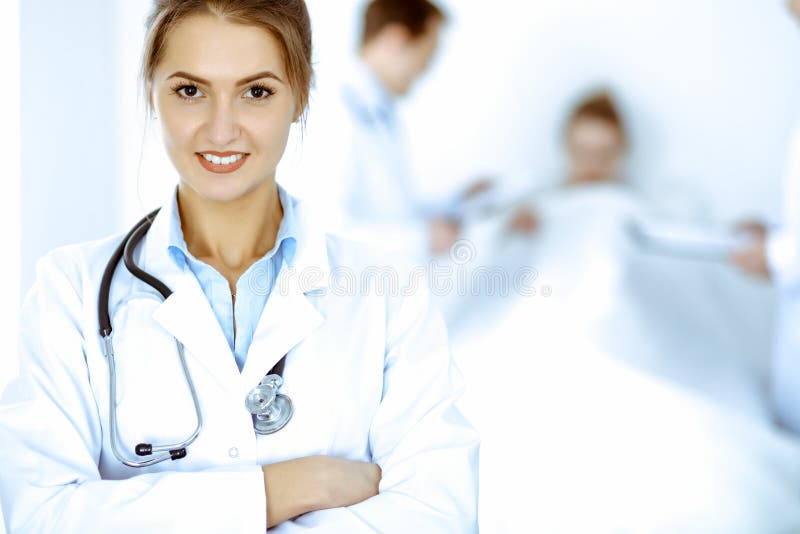 Kvinnor som leker i bakgrunden med patienten i sängen och två läkare arkivbild
