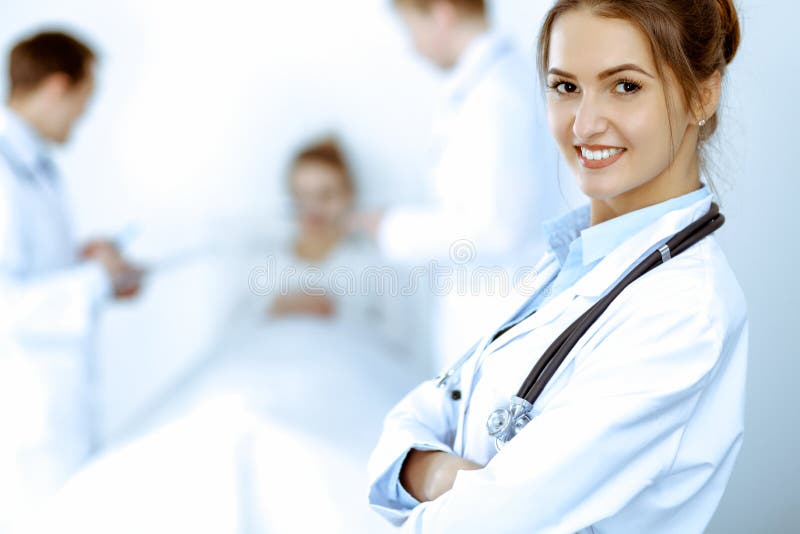Kvinnor som leker i bakgrunden med patienten i sängen och två läkare arkivbild