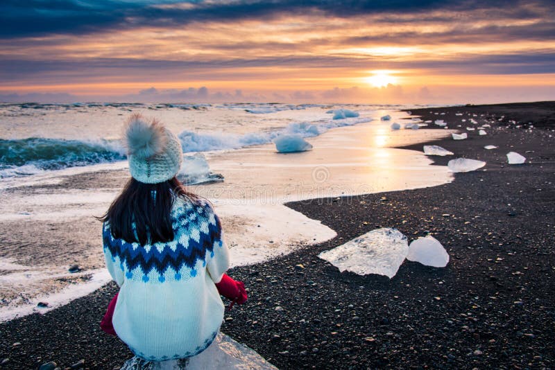 Woman sitting on iceberg and enjoying Diamond beach sunset in Iceland, arctic, traveler, people, water, icelandic, winter, glacier, melting, seaside, coast, person, crystal, female, girl, exploring, jokulsarlon, explorer, visitor, sweater, hat, tourist, wanderlust, ocean, glacial, sunrise, back, lagoon, rear, sky, wave, background, splash, outdoor, reykjavik, tourism, nature, europe. Woman sitting on iceberg and enjoying Diamond beach sunset in Iceland, arctic, traveler, people, water, icelandic, winter, glacier, melting, seaside, coast, person, crystal, female, girl, exploring, jokulsarlon, explorer, visitor, sweater, hat, tourist, wanderlust, ocean, glacial, sunrise, back, lagoon, rear, sky, wave, background, splash, outdoor, reykjavik, tourism, nature, europe