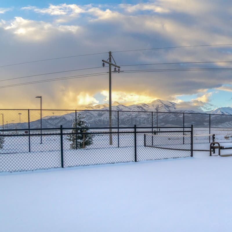 Square Tennis courts on a landscape blanketed with snow during winter season. A stunning snow capped mountain against cloudy sky at sunset can be seen in the distance. Square Tennis courts on a landscape blanketed with snow during winter season. A stunning snow capped mountain against cloudy sky at sunset can be seen in the distance.