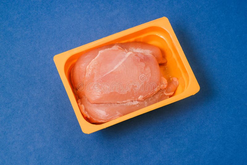 Kycklingsfilé i ett paket Råkött för matlagning Ställ in produkten i en behållare på en blå bakgrund Förbereda fågeln för royaltyfria bilder