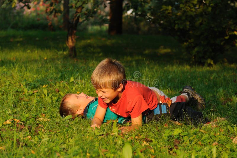 Young children, two boys, struggling in a garden, lying on grass and having fun. Young children, two boys, struggling in a garden, lying on grass and having fun