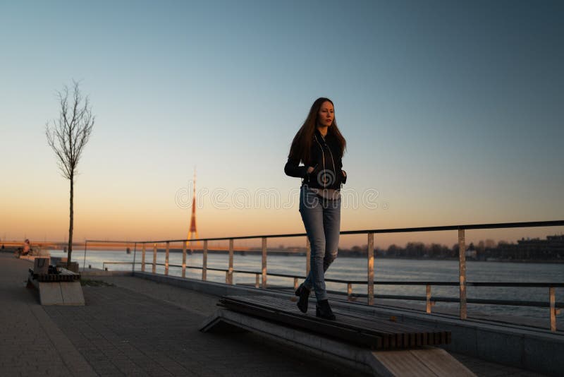 Känsla för den unga kvinnan som är säker under en livsstil, promenerar floddaugavaen på en solnedgång royaltyfria foton Känsla för den unga kvinnan som är säker under en livsstil, promenerar floddaugavaen på en solnedgång royaltyfria foton
