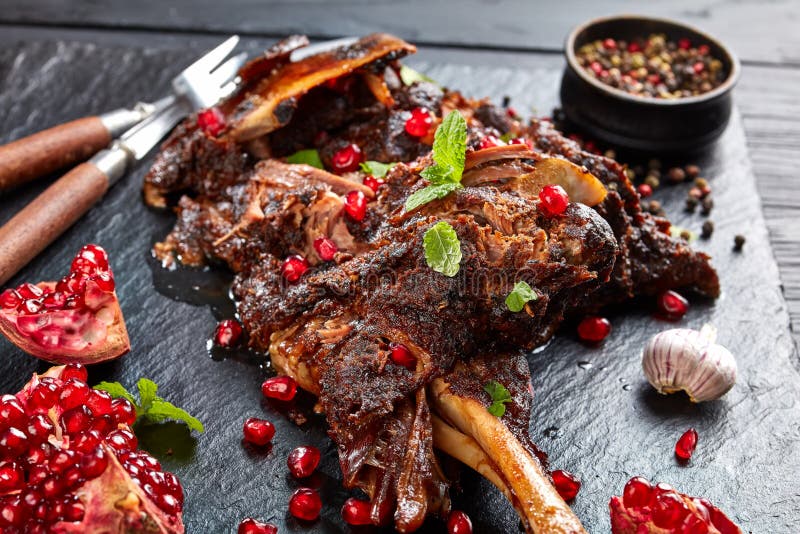 Köstliche langsame gekochte Lammkeule mit Granatapfelsamen, tadellosen Blättern, Gewürzen und Rosmarin auf einer schwarzen Schief lizenzfreies stockfoto Köstliche langsame gekochte Lammkeule mit Granatapfelsamen, tadellosen Blättern, Gewürzen und Rosmarin auf einer schwarzen Schief lizenzfreies stockfoto
