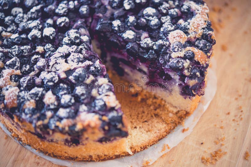 Köstlicher Blueberry-Kuchen mit abgeschnittenem Slice, mit kräftigen Farben und Texturen auf einer Holzfläche lizenzfreie stockfotos