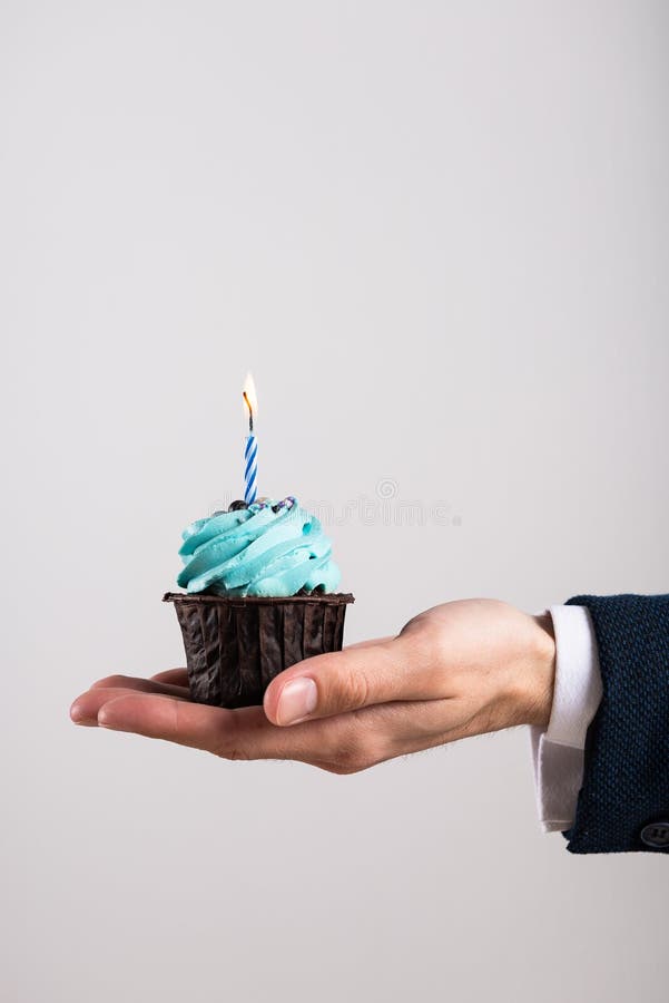 Delicious birthday cupcake with birning candle in businessman`s hand. Business greeting card. 1 year. Corporate party. Copy space for text. Delicious birthday cupcake with birning candle in businessman`s hand. Business greeting card. 1 year. Corporate party. Copy space for text