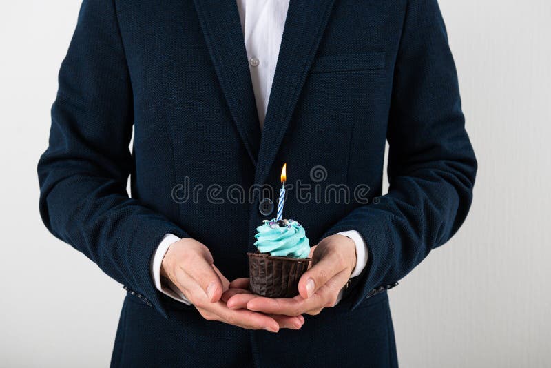 Delicious birthday cupcake with birning candle in businessman`s hand. Business greeting card. 1 year. Corporate party. Copy space for text. Delicious birthday cupcake with birning candle in businessman`s hand. Business greeting card. 1 year. Corporate party. Copy space for text