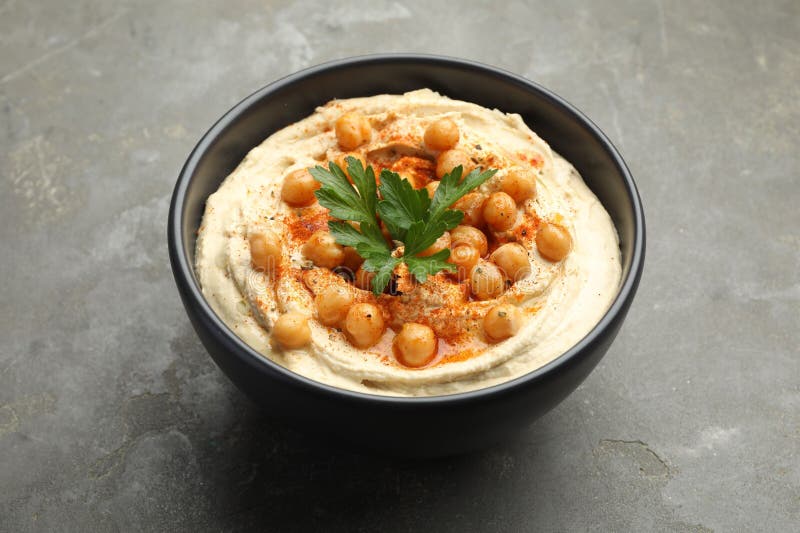 Köstlicher Hummus mit Petersilie Paprika und Kichererbsen in Schüssel auf grauem Tisch in der Nähe lizenzfreie stockfotos