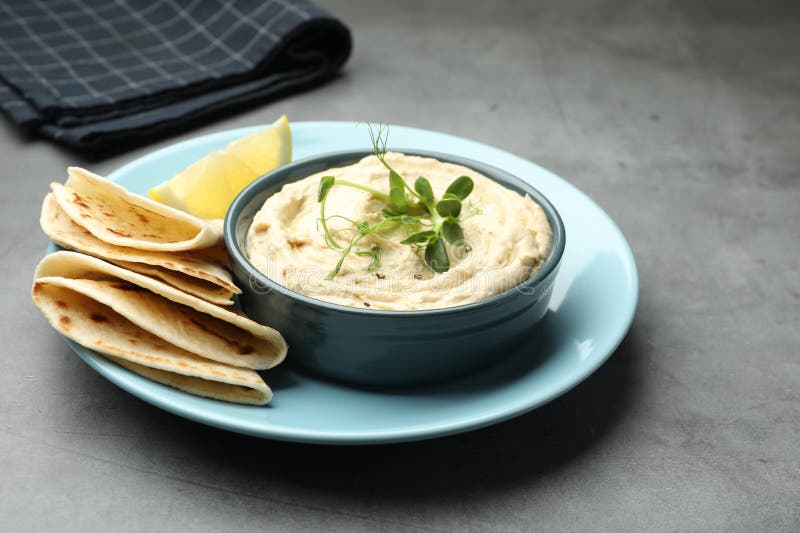Köstlicher Hummus in Schüssel Pita und Zitrone auf grauem Tisch in der Nähe stockfotografie