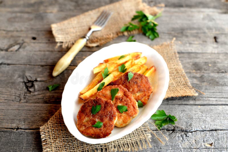 Köttkotletter och stekte potatisar på en platta, en gaffel, en kvist av persilja och säckväv på gammal wood bakgrund royaltyfria foton Köttkotletter och stekte potatisar på en platta, en gaffel, en kvist av persilja och säckväv på gammal wood bakgrund royaltyfria foton