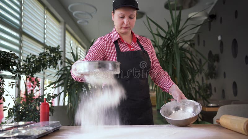 Küchenchef, der Mehl durch ein Sieb auf einem Tisch in einer italienischen Pizzeria schmiedet und Pizza-Teig backt. Kochbrot