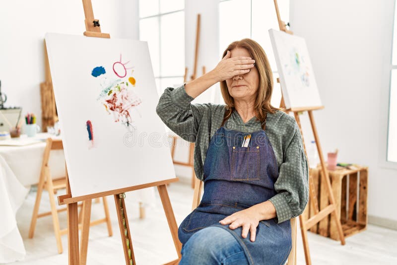 Middle age artist woman at art studio smiling and laughing with hand on face covering eyes for surprise. blind concept. Middle age artist woman at art studio smiling and laughing with hand on face covering eyes for surprise. blind concept