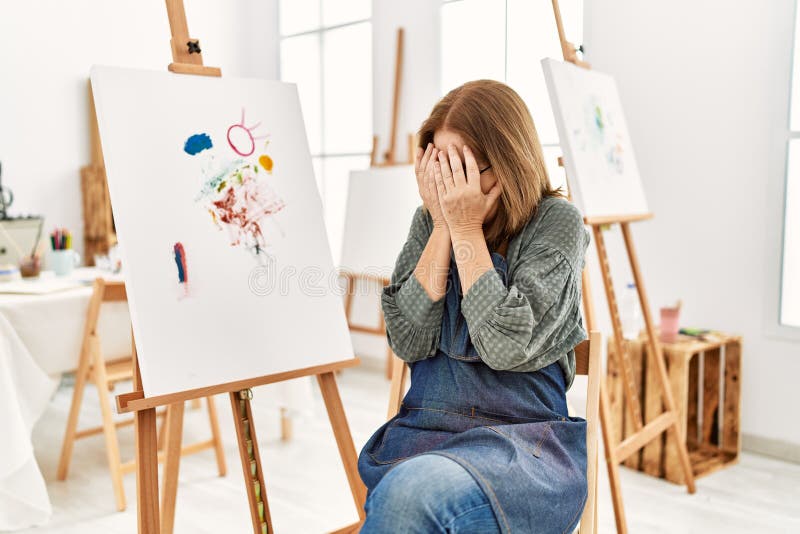 Middle age artist woman at art studio with sad expression covering face with hands while crying. depression concept. Middle age artist woman at art studio with sad expression covering face with hands while crying. depression concept