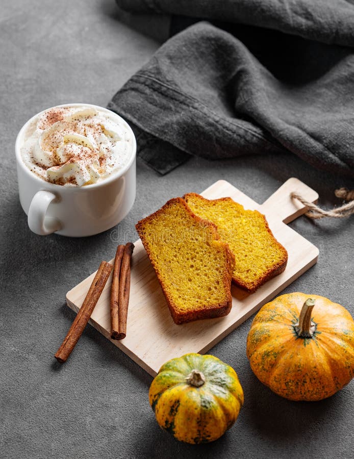 Kürbiskuchen mit Zimt auf einem Holzbrett auf dunklem Hintergrund mit dekorativen Kürbissen und einer Tasse heißem Kürbis stockfoto