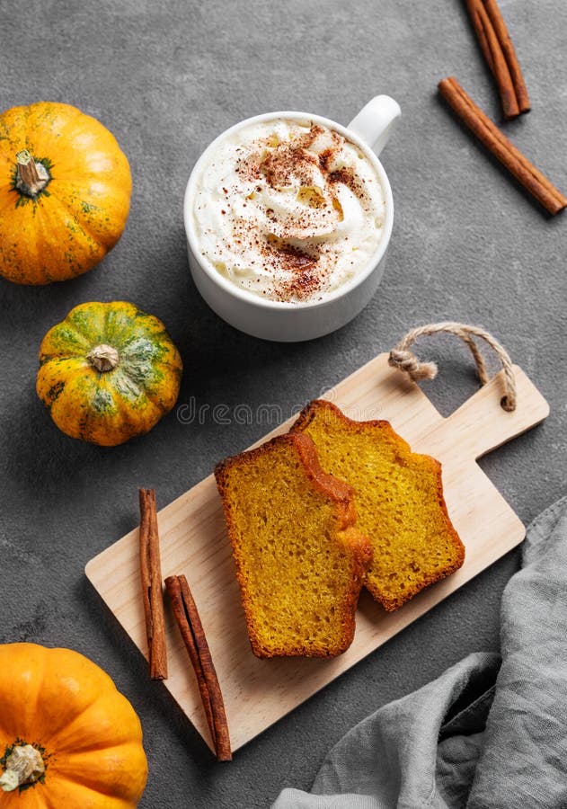 Kürbiskuchen mit Zimt auf einem Holzbrett auf dunklem Hintergrund mit dekorativen Kürbissen und einer Tasse heißem Kürbis stockfoto