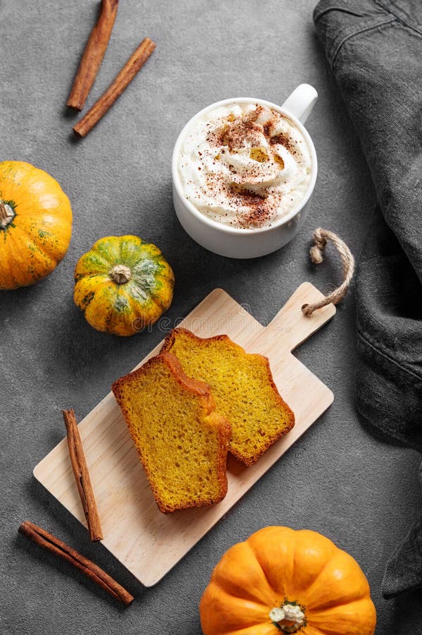 Kürbiskuchen mit Zimt auf einem Holzbrett auf dunklem Hintergrund mit dekorativen Kürbissen und einer Tasse heißem Kürbis stockfoto