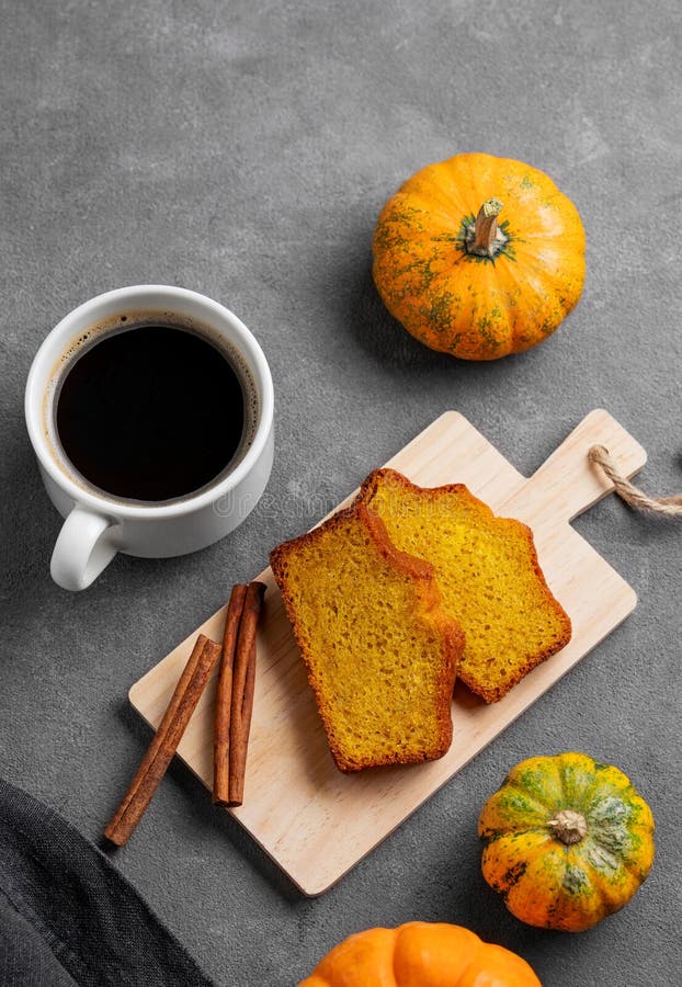 Kürbiskuchen mit Zimt auf einem Holzbrett auf dunklem Hintergrund mit dekorativen Kürbissen und einer Tasse Kaffee stockfoto
