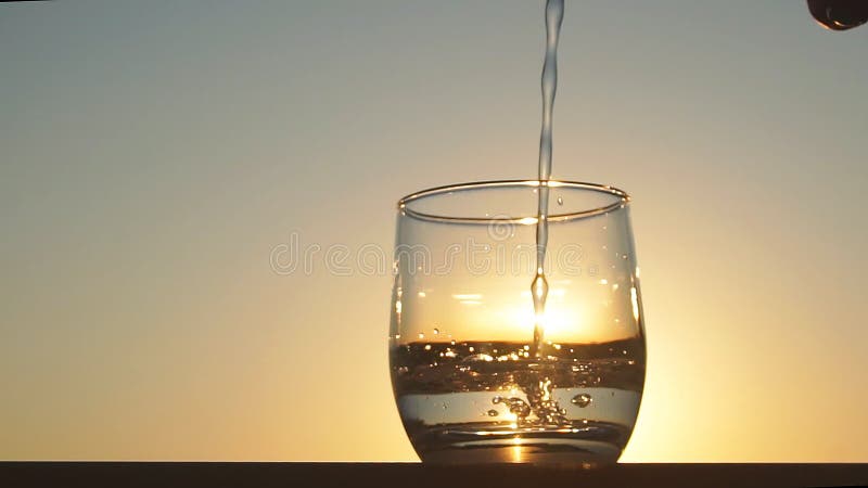 L'acqua dolce pulita e ha versato in un vetro al tramonto Movimento lento