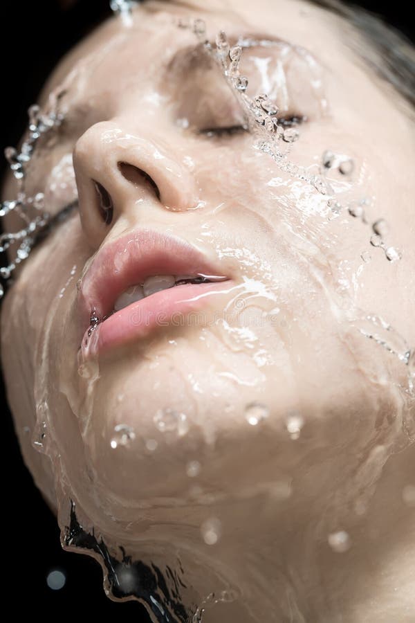 Amazing wet girl with closed eyes and parted lips on the black background in the studio. Water flows from her face. Closeup. Vertical. Amazing wet girl with closed eyes and parted lips on the black background in the studio. Water flows from her face. Closeup. Vertical.