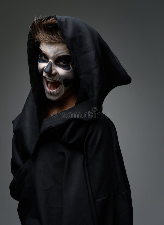 L'ado avec le maquillage du crâne dans le manteau noir rit photos stock L'ado avec le maquillage du crâne dans le manteau noir rit photos stock