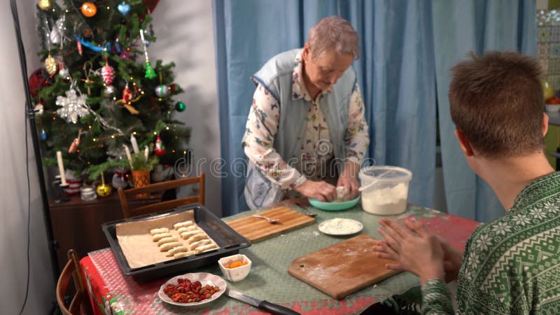 L'adolescent aide sa grand-mère à cuire des biscuits de Noël. Un garçon prépare la nourriture dans la cuisine. Faire un biscuit à clips vidéos