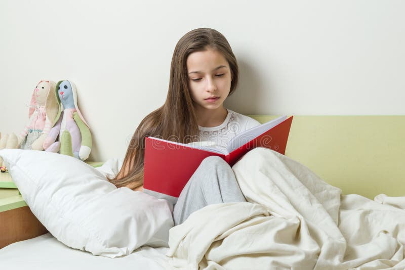 L'adolescente 10 années lit un carnet d'école sur le lit Intérieur de fond de la salle du ` s d'enfants photo libre de droits L'adolescente 10 années lit un carnet d'école sur le lit Intérieur de fond de la salle du ` s d'enfants photo libre de droits
