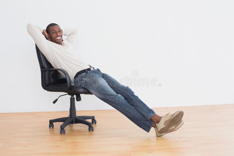 L'afro sorridente equipaggia la seduta sulla sedia dell'ufficio in una stanza vuota immagine stock L'afro sorridente equipaggia la seduta sulla sedia dell'ufficio in una stanza vuota immagine stock