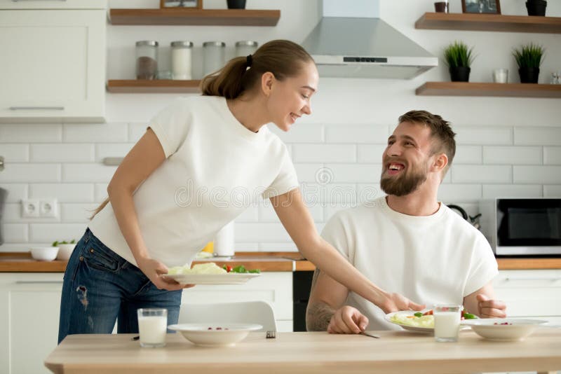 L'alimento attraente del servizio della moglie ha cucinato per il marito nella cucina fotografia stock L'alimento attraente del servizio della moglie ha cucinato per il marito nella cucina fotografia stock