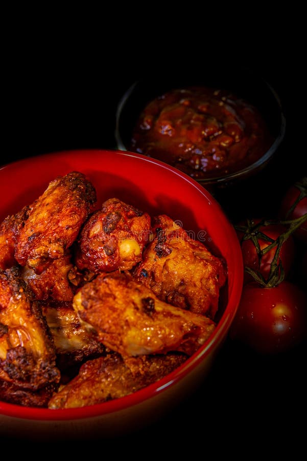L'Allemand grillé chiken les ailes, la sauce barbecue et les tomates au fond noir photos stock L'Allemand grillé chiken les ailes, la sauce barbecue et les tomates au fond noir photos stock