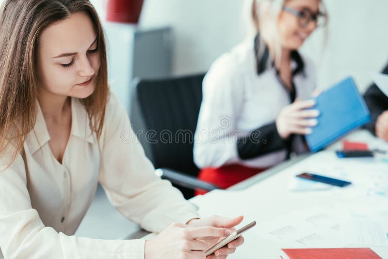 Bored at work. Team member slacking off. Woman browsing smartphone at workplace. Bored at work. Team member slacking off. Woman browsing smartphone at workplace.