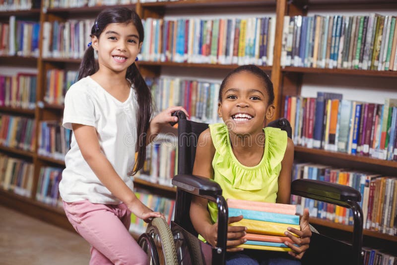 L'allievo sorridente nella tenuta della sedia a rotelle prenota nella biblioteca fotografie stock L'allievo sorridente nella tenuta della sedia a rotelle prenota nella biblioteca fotografie stock