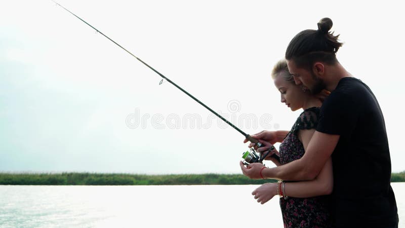 L'ami enseigne son amie à pêcher sur tourner par le bord de lac, équipent étreindre sa belle femme