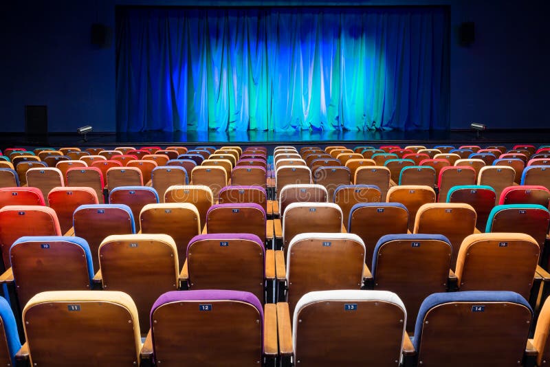 The auditorium in the theater. Blue-green curtain on the stage. Multicolored spectator chairs. Lighting equipment. The auditorium in the theater. Blue-green curtain on the stage. Multicolored spectator chairs. Lighting equipment.