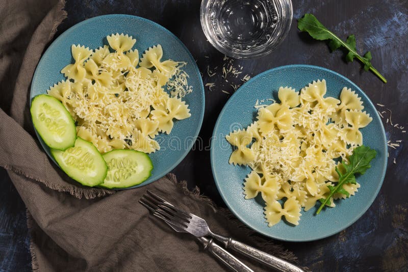 L'arco della pasta è spruzzato con formaggio, le foglie di rucola, il cetriolo fresco, fondo blu scuro immagine stock L'arco della pasta è spruzzato con formaggio, le foglie di rucola, il cetriolo fresco, fondo blu scuro immagine stock