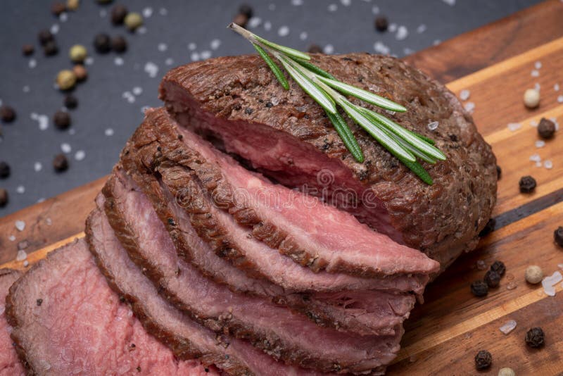 L'arrosto di manzo succoso allevato ad erba affettato del cereale ha guarnito con Rosemary Herb ed i granelli di pepe freschi del immagini stock libere da diritti L'arrosto di manzo succoso allevato ad erba affettato del cereale ha guarnito con Rosemary Herb ed i granelli di pepe freschi del immagini stock libere da diritti