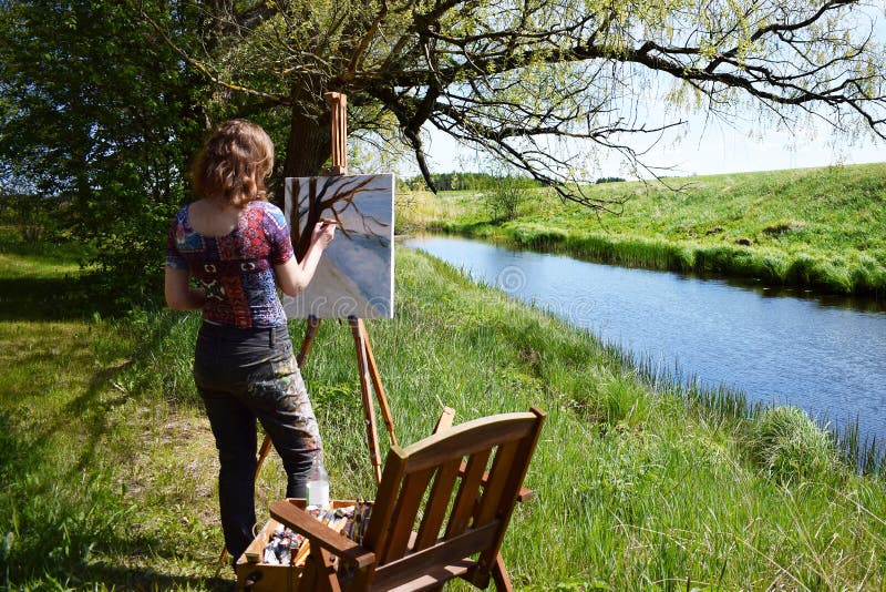 L'artiste de femme peint la peinture de paysage de la petite rivière images stock L'artiste de femme peint la peinture de paysage de la petite rivière images stock