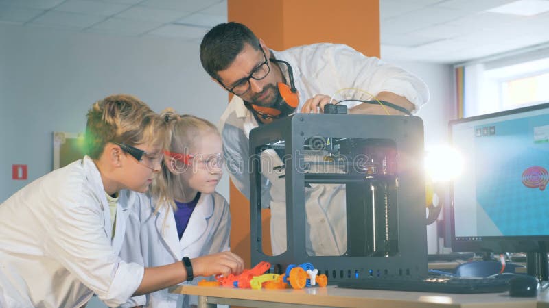 L'associé de laboratoire démontre le processus fonctionnant d'une imprimante 3D aux enfants