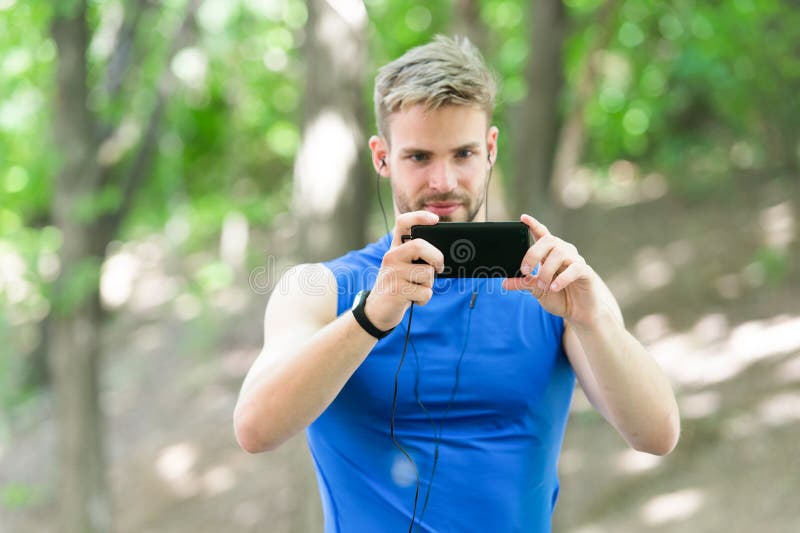 L'athlète d'homme a concentré le fond de nature de photo de smartphone de prise de visage Podomètre et écouteurs de formation de photographie stock libre de droits L'athlète d'homme a concentré le fond de nature de photo de smartphone de prise de visage Podomètre et écouteurs de formation de photographie stock libre de droits