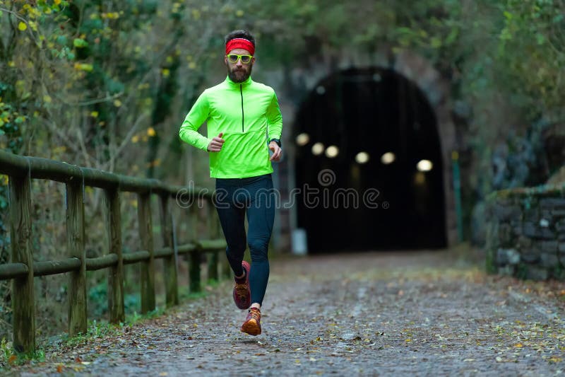L'athlète d'homme court sur le chemin de vélo entre les tunnels en automne photo stock L'athlète d'homme court sur le chemin de vélo entre les tunnels en automne photo stock