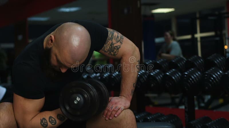 L'athlète masculin musculaire tatoué faisant l'haltère s'exerce, établissant dans le gymnase