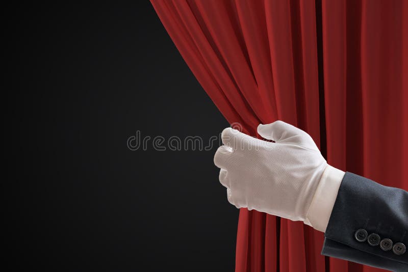 L'attore sta tirando le tende rosse nel teatro con la mano fotografia stock L'attore sta tirando le tende rosse nel teatro con la mano fotografia stock