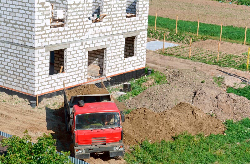 L'autocarro con cassone ribaltabile vicino alla casa in costruzione, il camion e la costruzione della casa da un mattone bianco, fotografie stock L'autocarro con cassone ribaltabile vicino alla casa in costruzione, il camion e la costruzione della casa da un mattone bianco, fotografie stock