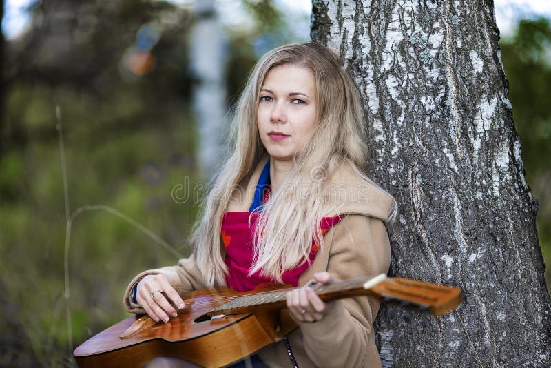 L'autunno triste è il biondo con la chitarra che si siede sulla terra da un albero di betulla fotografia stock libera da diritti L'autunno triste è il biondo con la chitarra che si siede sulla terra da un albero di betulla fotografia stock libera da diritti