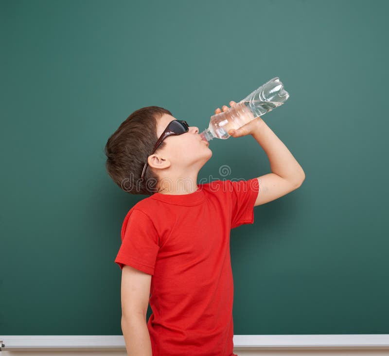 L'eau de boissons d'écolier de la bouteille près d'un tableau noir, l'espace vide, concept d'éducation photos stock L'eau de boissons d'écolier de la bouteille près d'un tableau noir, l'espace vide, concept d'éducation photos stock