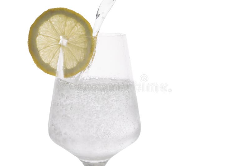 L'eau de scintillement étant versée dans un verre avec une tranche de citron photographie stock L'eau de scintillement étant versée dans un verre avec une tranche de citron photographie stock