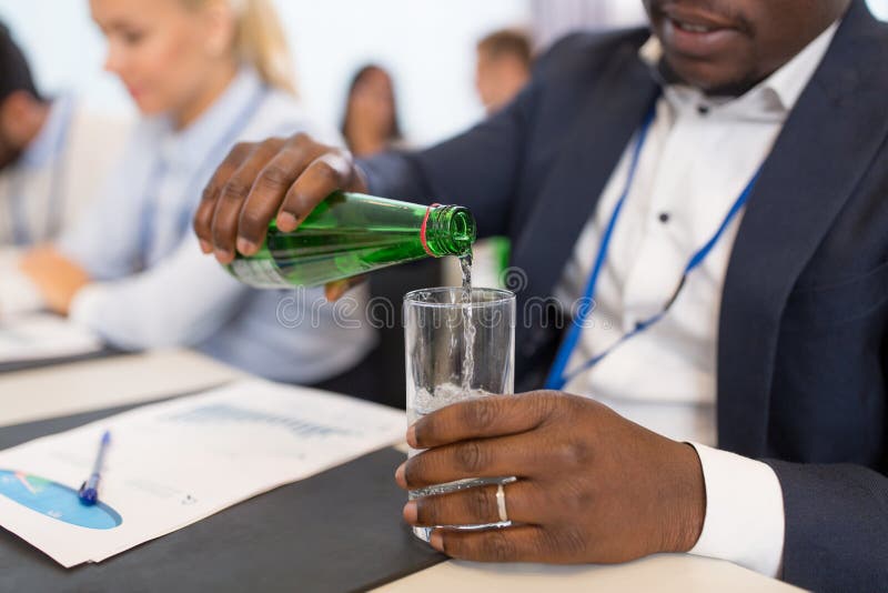 L'eau de versement d'homme d'affaires au verre à la conférence image stock L'eau de versement d'homme d'affaires au verre à la conférence image stock